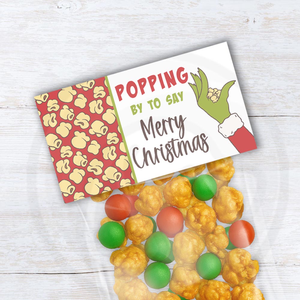 Printable Christmas popcorn bag topper with red background and green cartoon hand. Red holiday treat bag topper saying “Popping by to say Merry Christmas”
