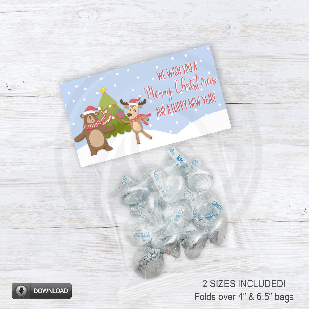 Printable Christmas treat bag topper featuring a cute reindeer and bear in scarves dancing by a Christmas tree with “We wish you a Merry Christmas and a Happy New Year” text on a snowy blue background.