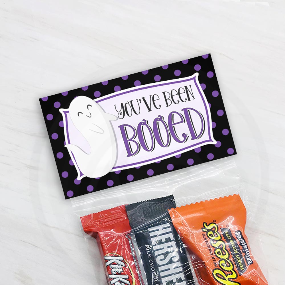 Printable Halloween bag topper with “You’ve Been Booed” wording, a smiling white ghost, and a black border covered in purple polka dots, available for 4" and 6.5" bags.