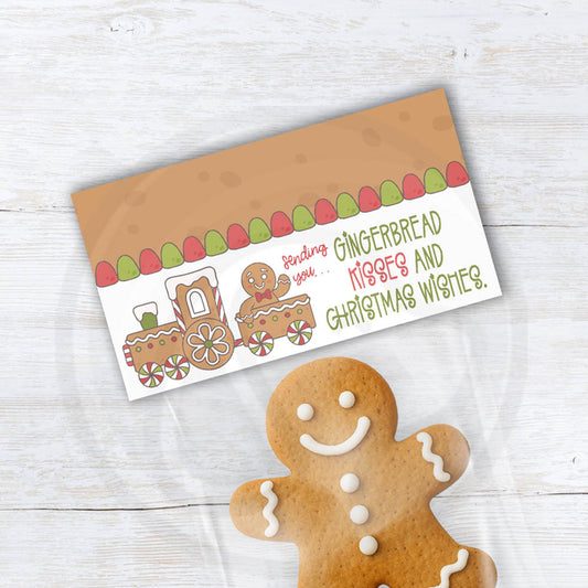 Printable gingerbread bag topper featuring a cute gingerbread train with gumdrop border and the phrase “Sending you gingerbread kisses and Christmas wishes,” folded over a clear treat bag with a gingerbread cookie.